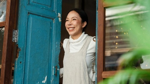 An Asian woman smiling and opening a door